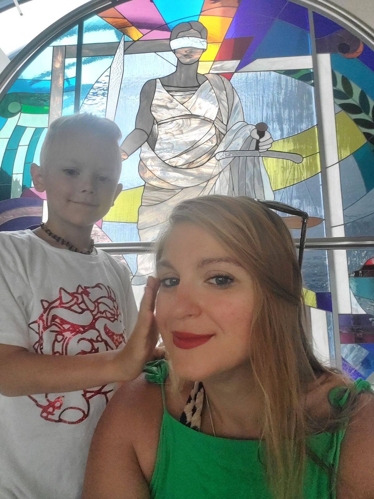 Mutter und Sohn, glücklich, vor einem Kirchenfenster mit der Justitia-Darstellung